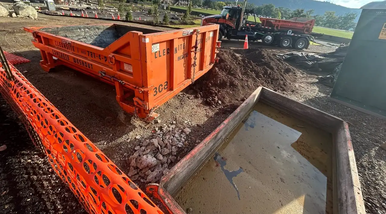 CleanSite washout container and a pan holding washout water behind orange safety fence