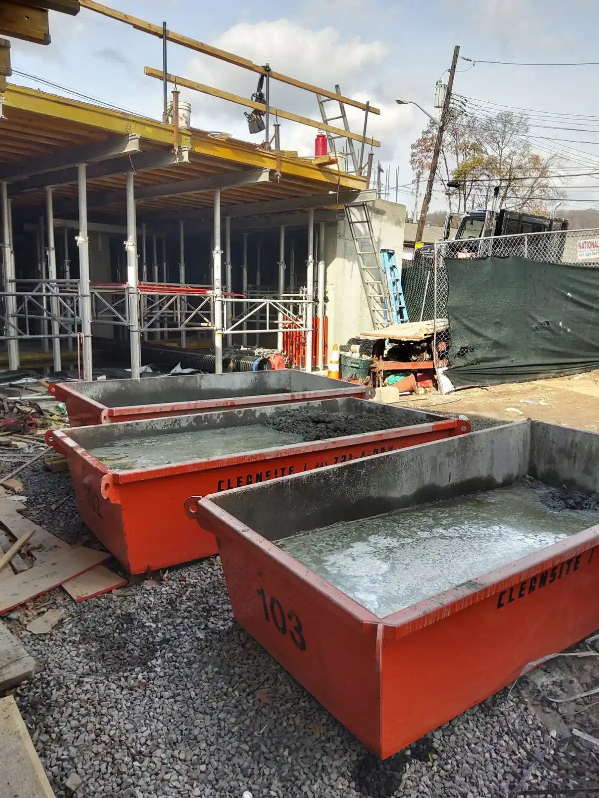 Three CleanSite washout pans holding washout water beside a building under construction